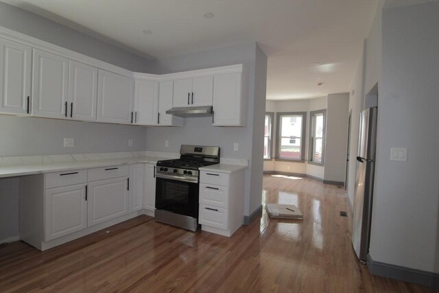 kitchen with under cabinet range hood, white cabinets, appliances with stainless steel finishes, and wood finished floors