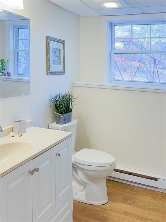 half bath with vanity, wood finished floors, a paneled ceiling, toilet, and baseboard heating