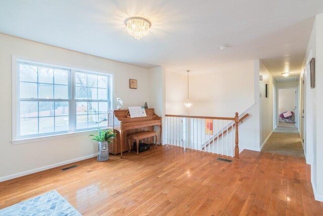 hall with hardwood / wood-style floors, an upstairs landing, visible vents, and baseboards