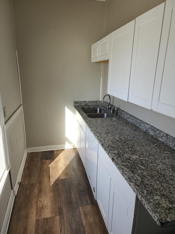 kitchen with stone countertops, a sink, baseboards, white cabinets, and dark wood-style floors