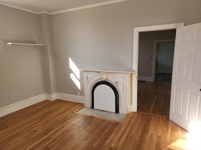 unfurnished living room with baseboards, a fireplace with flush hearth, hardwood / wood-style flooring, and crown molding