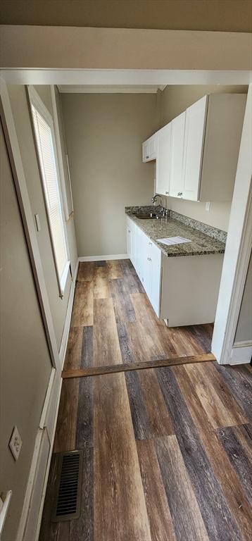 kitchen with a sink, visible vents, wood finished floors, white cabinetry, and baseboards