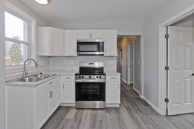 kitchen with sink, light wood-type flooring, white cabinets, and appliances with stainless steel finishes