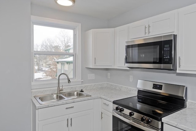 kitchen with stainless steel appliances, white cabinetry, sink, and light stone counters