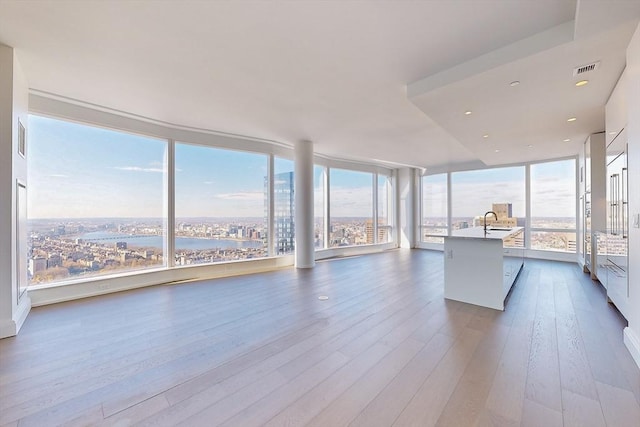 interior space featuring a center island with sink, hardwood / wood-style floors, a wealth of natural light, floor to ceiling windows, and white cabinets