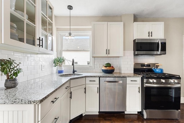 kitchen with light stone counters, a sink, white cabinets, appliances with stainless steel finishes, and glass insert cabinets