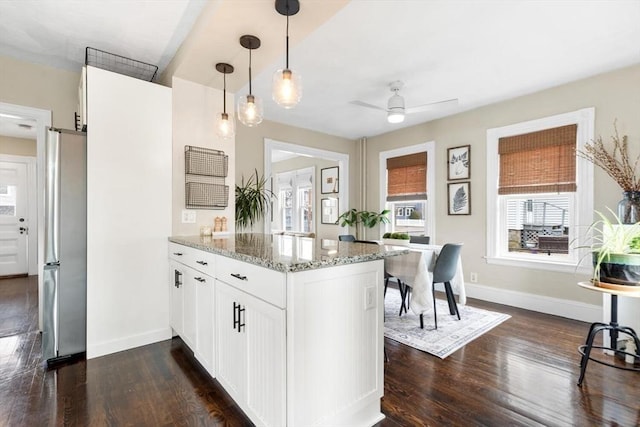 kitchen featuring dark wood-style floors, freestanding refrigerator, a peninsula, light stone countertops, and white cabinetry