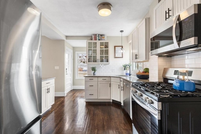 kitchen featuring stainless steel appliances, a sink, light stone countertops, dark wood-style floors, and glass insert cabinets