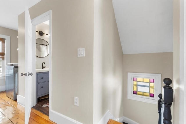 hallway featuring baseboards, a sink, and light wood finished floors