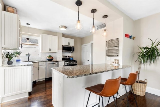 kitchen with decorative backsplash, appliances with stainless steel finishes, dark wood-type flooring, a peninsula, and a sink