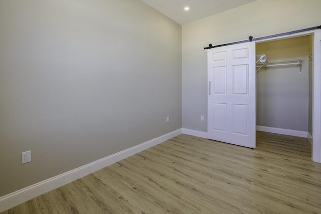 unfurnished bedroom featuring light wood-style floors, a closet, baseboards, and a barn door