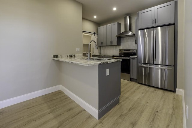 kitchen featuring stainless steel appliances, a barn door, a sink, wall chimney range hood, and a peninsula