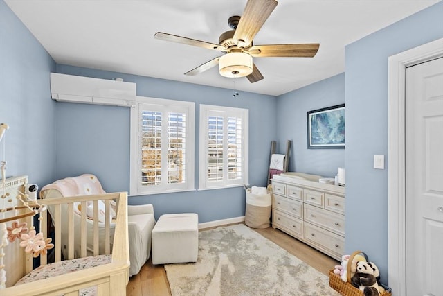 bedroom with ceiling fan, an AC wall unit, and light wood-type flooring