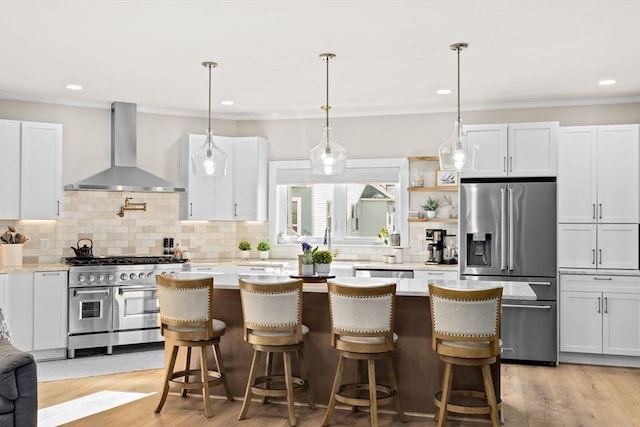 kitchen with high quality appliances, a breakfast bar area, wall chimney range hood, and white cabinets