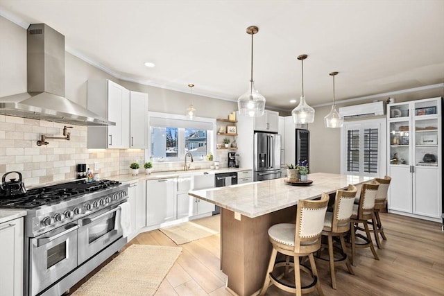 kitchen featuring wall chimney range hood, white cabinetry, light stone counters, premium appliances, and a kitchen island