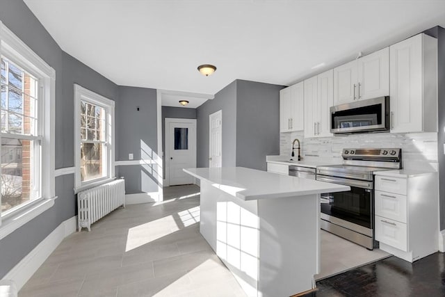 kitchen featuring white cabinets, light countertops, appliances with stainless steel finishes, tasteful backsplash, and radiator heating unit