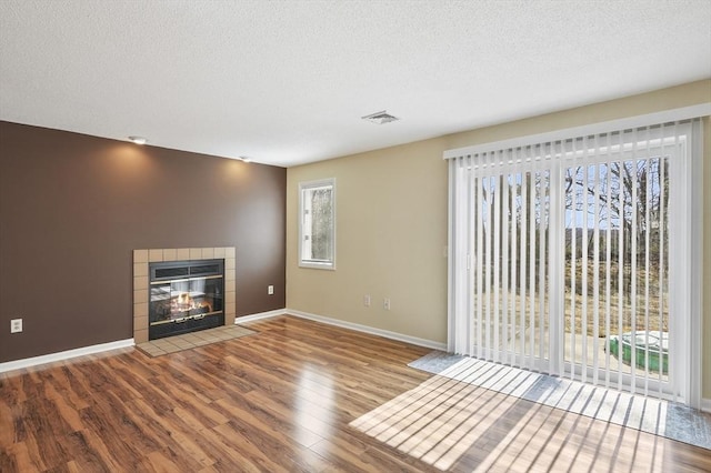 unfurnished living room featuring visible vents, a textured ceiling, wood finished floors, baseboards, and a tile fireplace