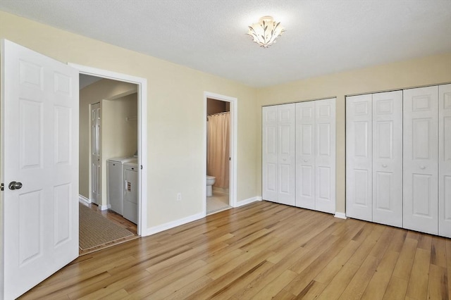 unfurnished bedroom featuring light wood-type flooring, two closets, washer and clothes dryer, connected bathroom, and baseboards