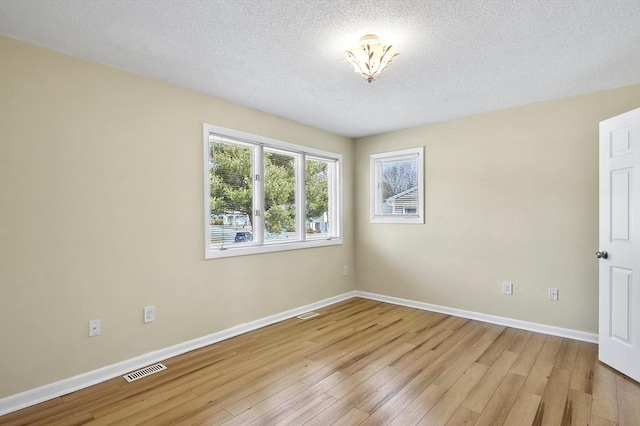 empty room featuring a textured ceiling, baseboards, visible vents, and light wood-type flooring