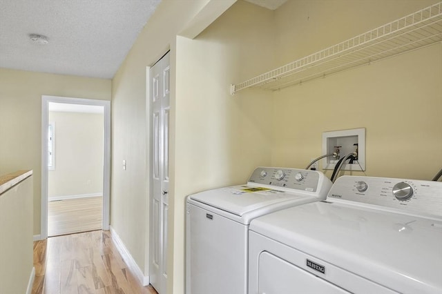 laundry room featuring washing machine and clothes dryer, laundry area, light wood finished floors, and a textured ceiling