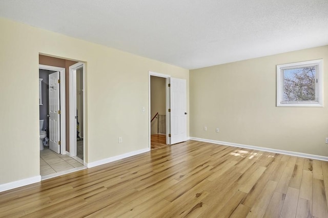 unfurnished bedroom with baseboards, light wood-style floors, ensuite bath, and a textured ceiling