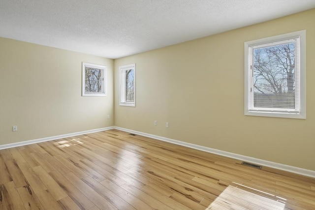 unfurnished room with light wood-type flooring, visible vents, baseboards, and a textured ceiling