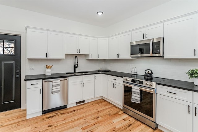 kitchen featuring white cabinetry, sink, tasteful backsplash, light hardwood / wood-style flooring, and appliances with stainless steel finishes