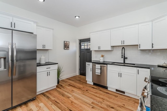 kitchen with sink, backsplash, appliances with stainless steel finishes, white cabinets, and light wood-type flooring