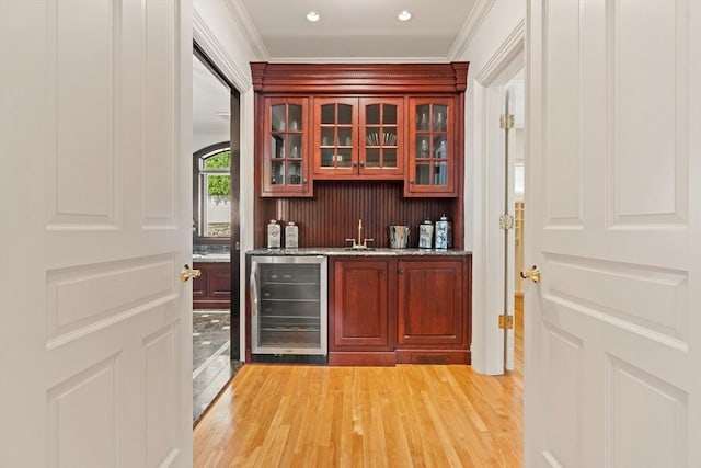 bar with light wood-style floors, crown molding, indoor wet bar, and beverage cooler