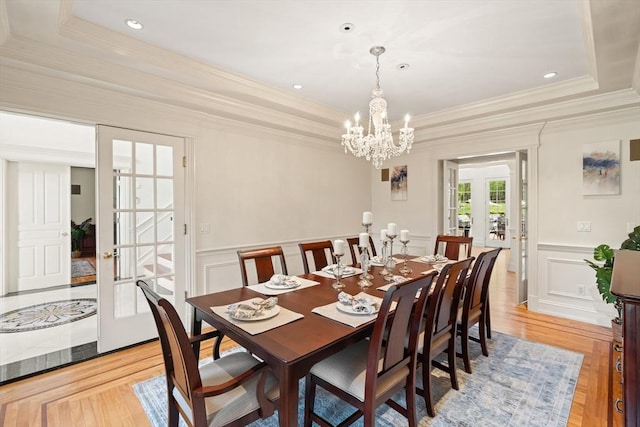 dining area with an inviting chandelier, a raised ceiling, ornamental molding, and french doors