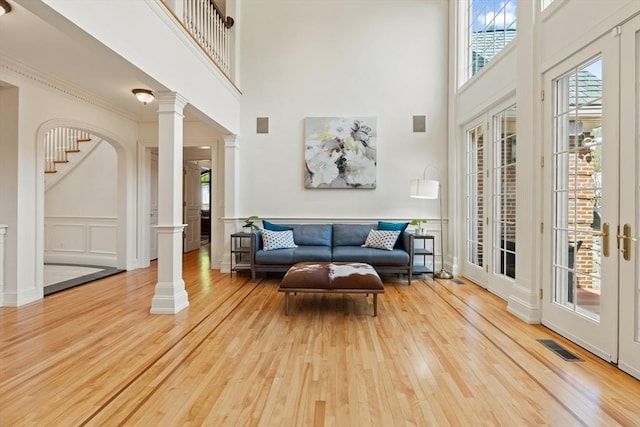living room featuring decorative columns, visible vents, wood finished floors, a high ceiling, and stairs