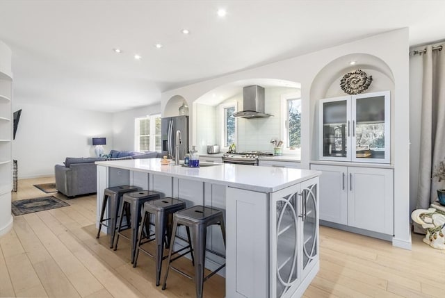 kitchen featuring light countertops, light wood-style flooring, wall chimney exhaust hood, and stainless steel appliances