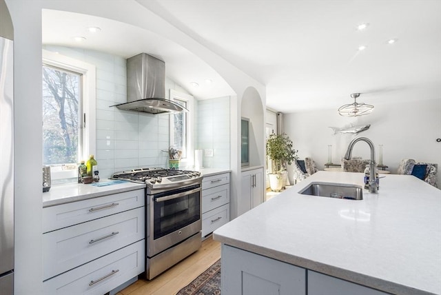 kitchen featuring tasteful backsplash, stainless steel range with gas stovetop, light wood-style flooring, wall chimney exhaust hood, and a sink