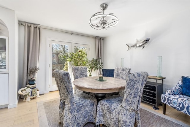 dining space with light wood-style flooring, french doors, and an inviting chandelier