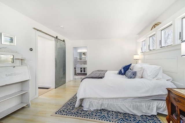 bedroom featuring a barn door, light wood-style flooring, and connected bathroom