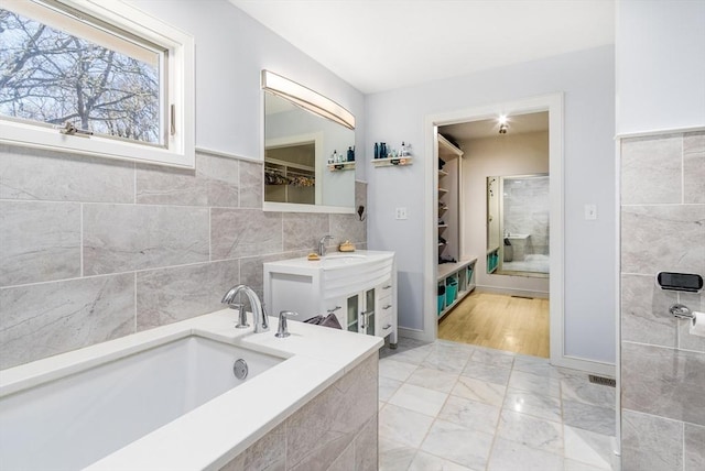 full bath with vanity, a spacious closet, tiled bath, tile walls, and marble finish floor