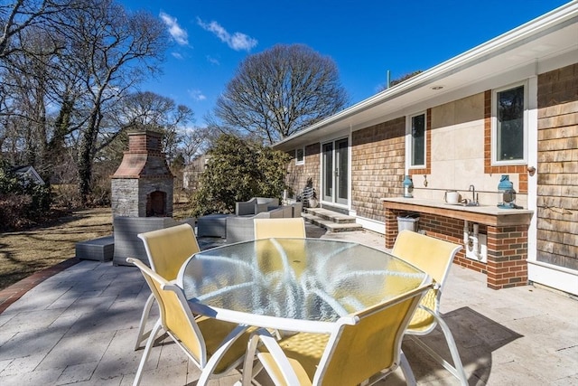 view of patio / terrace featuring outdoor dining space, an outdoor fireplace, entry steps, and a sink