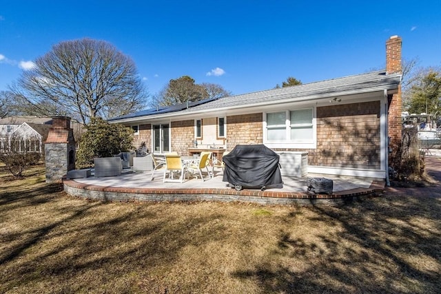 back of house featuring solar panels, a patio area, a lawn, and a chimney