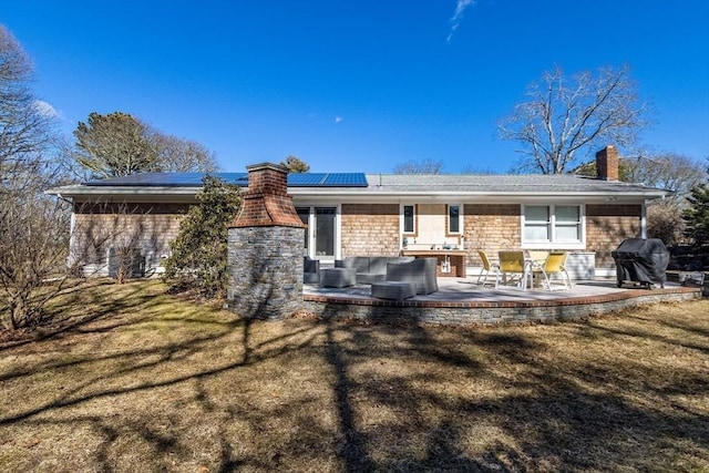 back of property featuring a patio area, a lawn, roof mounted solar panels, and a chimney