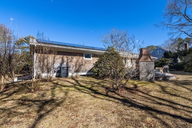 back of house with roof mounted solar panels, a lawn, and central AC