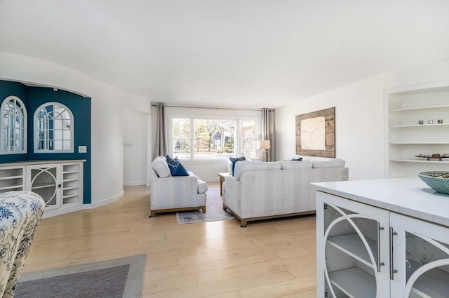 living area featuring light wood-style flooring, built in shelves, and baseboards