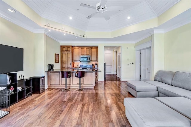 living room with a raised ceiling, crown molding, hardwood / wood-style flooring, and ceiling fan