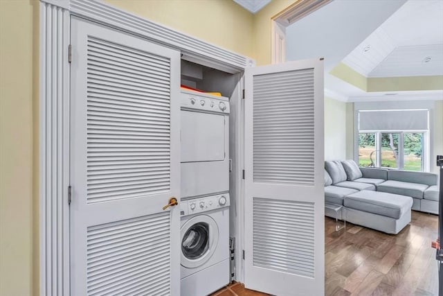 laundry area featuring stacked washer / dryer, ornamental molding, and wood-type flooring