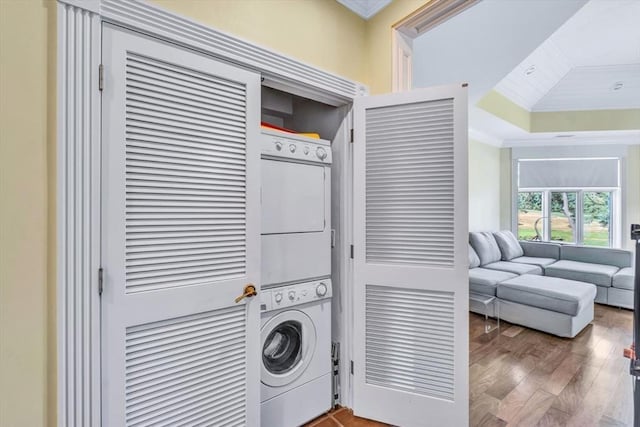 laundry room with stacked washer and dryer, ornamental molding, and wood-type flooring