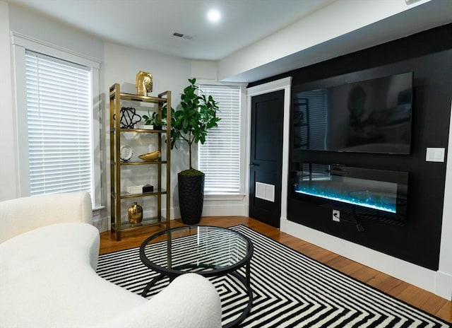 living room featuring a glass covered fireplace, wood finished floors, and visible vents