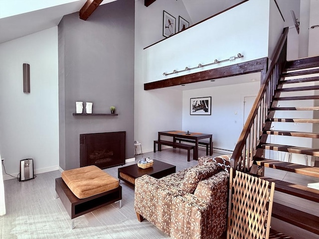 living area featuring beam ceiling, high vaulted ceiling, a fireplace, baseboards, and stairs