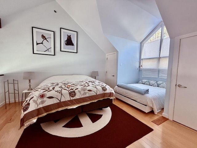 bedroom featuring baseboards, light wood-style floors, and vaulted ceiling