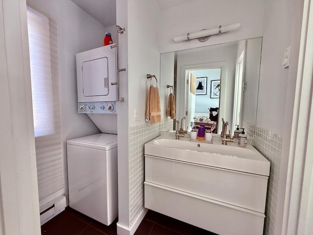 ensuite bathroom with tile patterned flooring, tile walls, stacked washing maching and dryer, ensuite bath, and vanity