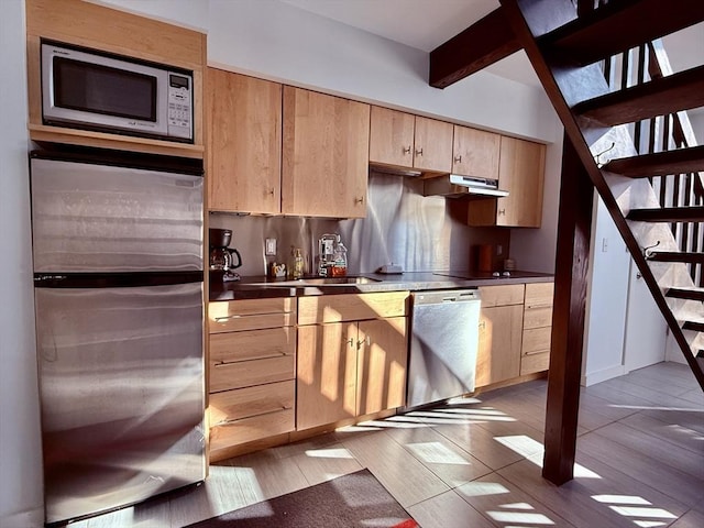 kitchen with dark countertops, light brown cabinets, under cabinet range hood, beam ceiling, and appliances with stainless steel finishes