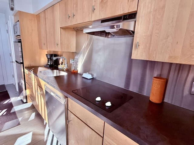 kitchen featuring light brown cabinetry, under cabinet range hood, a sink, dark countertops, and stainless steel appliances